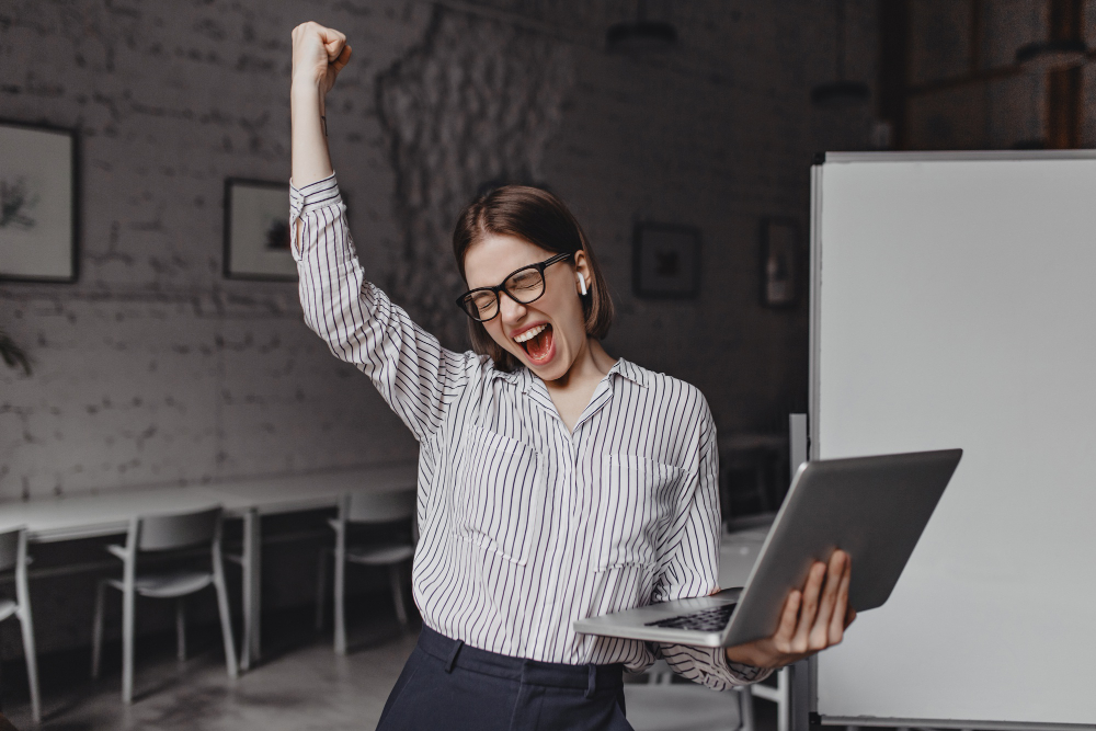 mujer negocios ordenador portatil mano feliz exito retrato mujer gafas blusa rayas gritando entusiasmo haciendo gesto ganador